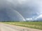 Rainbow over a road and grass field road with cloudy skies