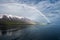 The rainbow over the sea near the snowy mountains and an isolated ship