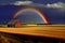 A rainbow over a wheat field, a small farmhouse in the distance. AI generated