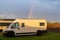 Rainbow in an overcast sky in golden evening light leading down to parked camper vans