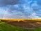 Rainbow in an overcast sky in golden evening light over freshly plowed farm field