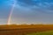 Rainbow in an overcast sky in golden evening light over freshly plowed farm field