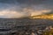 Rainbow shining through dark storm clouds with view of waves on lake