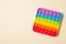 Rainbow silicone sensory antistress pop it toy on light brown background. Top view.