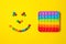 Rainbow silicone sensory antistress pop it toy with smiley from colorful candies on yellow background.