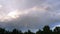 Rainbow in the sky with clouds above the trees.