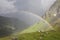 Rainbow stretching over a mountain valley in front of dark thunder storm.