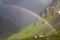 Rainbow stretching over a mountain valley in front of dark thunder storm-