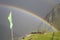 Rainbow stretching over a mountain valley in front of dark thunder storm.