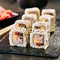 Rainbow uramaki sushi rolls with rice, bacon, processed cheese, tomato, green onion, sesame and nori on black slate plate backgrou