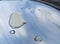 Raindrops on a shiny metal surface outside a room with a blue sky shadow