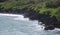 The rainforest lined, black volcanic rocky shoreline with tourists sight seeing at Waianapanapa State Park