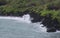 The rainforest lined, black volcanic rocky shoreline with tourists sight seeing at Waianapanapa State Park