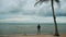 Rainy season in Thailand. Travel man standing on beach with palm tree