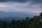 Rainy sunset in mountains with dark gloomy blue rain clouds, pink sky and sunlight over blue mountains silhouettes, green tropical