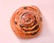 Raisin snail bun with icing sugar close-up on light pink background