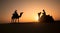 Rajasthan travel background - two indian cameleers camel drivers with camels silhouettes in dunes of Thar desert on sunset. Jais