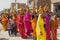 Rajasthani women wearing yellow and red sarees holding coconuts and pots take part in a religious procession in Bikaner, India.