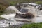 Rally car boosts water hurdle surrounded by splashes.