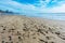 Random foot steps from shoes on sandy beach. Ocean waves, blue cloudy sky and coastline with residential buildings in background