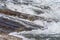 Rapid spring river flowing over rocks on sunny day, forming white water waves, closeup detail - abstract nature background