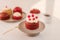 Raspberry cupcake on stand with a plate of various muffins on white background