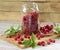 Raspberry in a glass jam jar with fresh leaves and berries scattered around on wooden cutting board