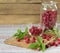 Raspberry in a glass jam jar with fresh leaves and berries scattered around on wooden cutting board