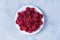 Raspberry plate is white on a gray table top view. Ripe raspberries in close-up