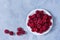 Raspberry plate is white on a gray table top view. Ripe raspberries in close-up