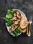 Ratatouille stuffed baked eggplant with mozzarella cheese, spinach and grilled bread on a dark background, top view