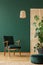 Rattan armchair above retro dark green armchair, copy space on the empty green wall