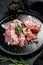 Raw bacon on a black plate, pepper and rosemary. Farm organic meat. Black background. Top view