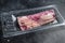 Raw beef bacon in vacuum packaging. Black background. Top view