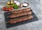 Raw beef lamb lula kebab on wooden skewer on a black stone surface, close up