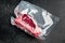 Raw beef meat Club or striploin on the bone steak in plastic airtight pack, on black stone background, with copy space for text