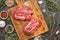 Raw beef meat on a cutting board with herbs and spices. View from above.