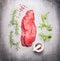 Raw beef meat steak with fresh herbs on gray stone background