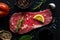 Raw beef meat, uncooked steak with rosemary, lemon and spices on black