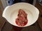 Raw beef with red liquid in white bowl or container in kitchen