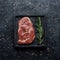 Raw beef rib eye steak with rosemary on black background top view. Square crop.