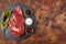 Raw beef ribeye on a round slate plate with glass containers containing peppercorns, coarse salt and cayenne chillies on an old