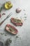 Raw beef steak with rosemary and green pepper on grey concrete kitchen table with butcher fork, olive oil and garlic. Preparing