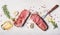 Raw beef Striploin steaks with oil , spices and meat fork on white stone background, top view, flat lay