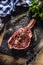 Raw beef tomahawk steak with salt pepper and rosemary on slate plate