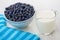 Raw blueberry in glass bowl, jug of milk, striped napkin