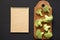 Raw broccoli pieces on rustic wooden board, blank notepad over black background, top view. From above, flat lay, from above