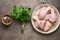Raw chicken drumstick on a plate, spices, a bunch of parsley arranged in a row. Dark rustic background, top view