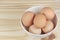 Raw chicken eggs in a white bowl on wooden table, horizontal view.