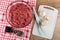 Raw chicken forcemeat in bowl, condiment in jar on napkin, garlic, knife on cutting board on wooden table. Top view